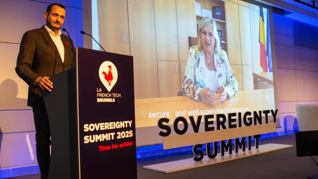 Samuel Profumo, président de La French Tech Brussels, au pupitre, avec la ministre belge Vanessa Matz à l'écran pendant son message vidéo au Summit 2025
