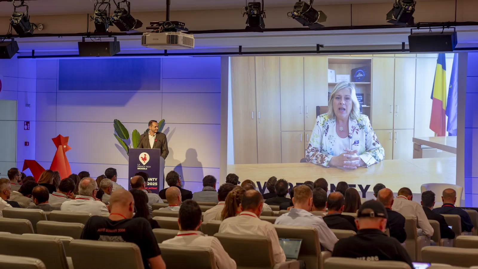 Le public de Square Brussels regarde le message vidéo de la ministre belge Vanessa Matz, avec Samuel Profumo sur scène